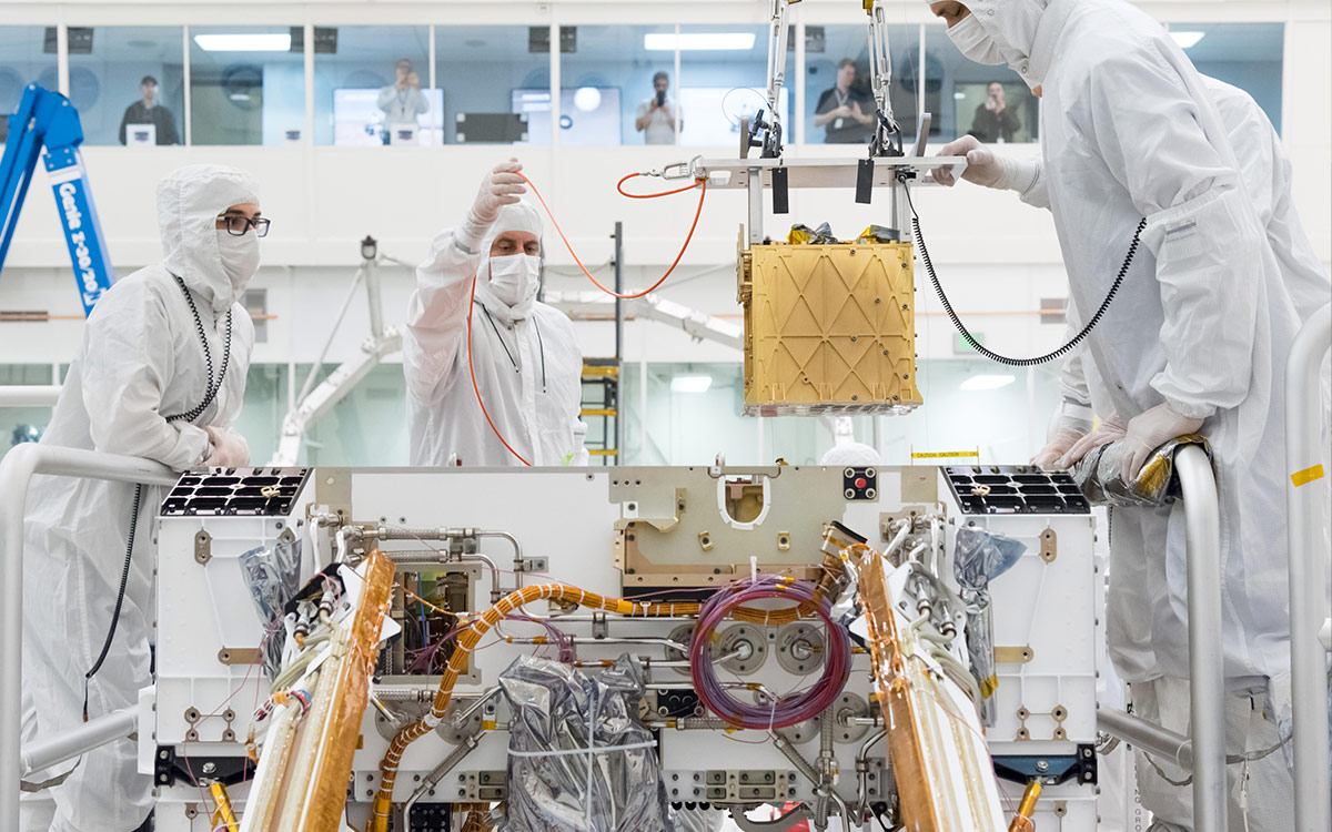 Technicians in the clean room are carefully lowering the Mars Oxygen In-Situ Resource Utilization Experiment (MOXIE) instrument into the belly of the Perseverance rover. Credit: NASA/JPL-Caltech